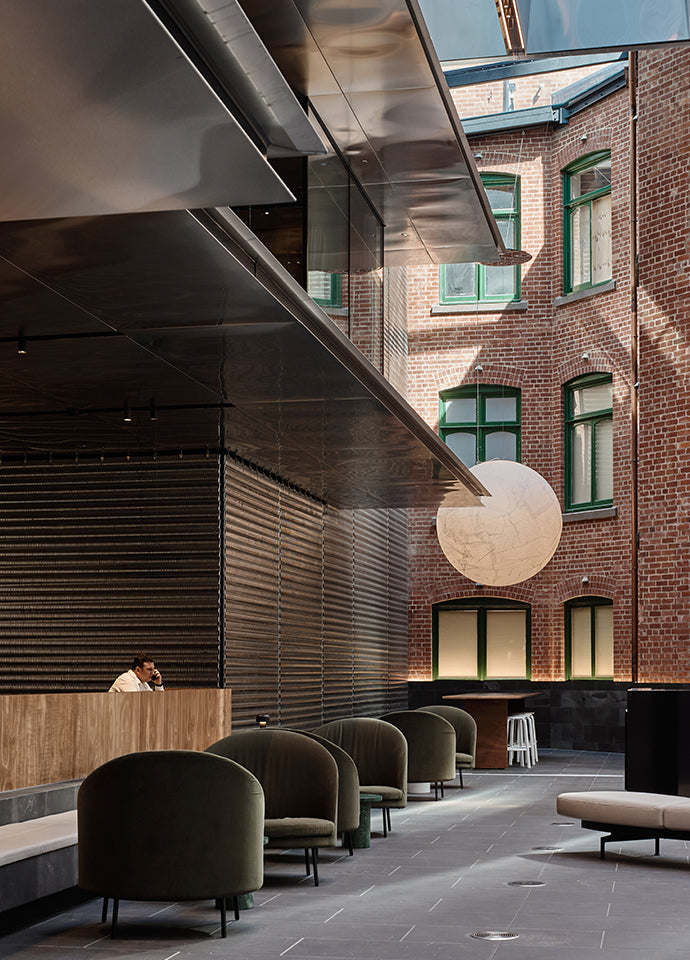 All textures and warm colour, the raw red bricks of a neighbouring building are offset by the Jim armchair in a forest green velvet by Arflex and the Container table in wood by Moooi. Photography © Peter Bennetts c/o Hassell.
